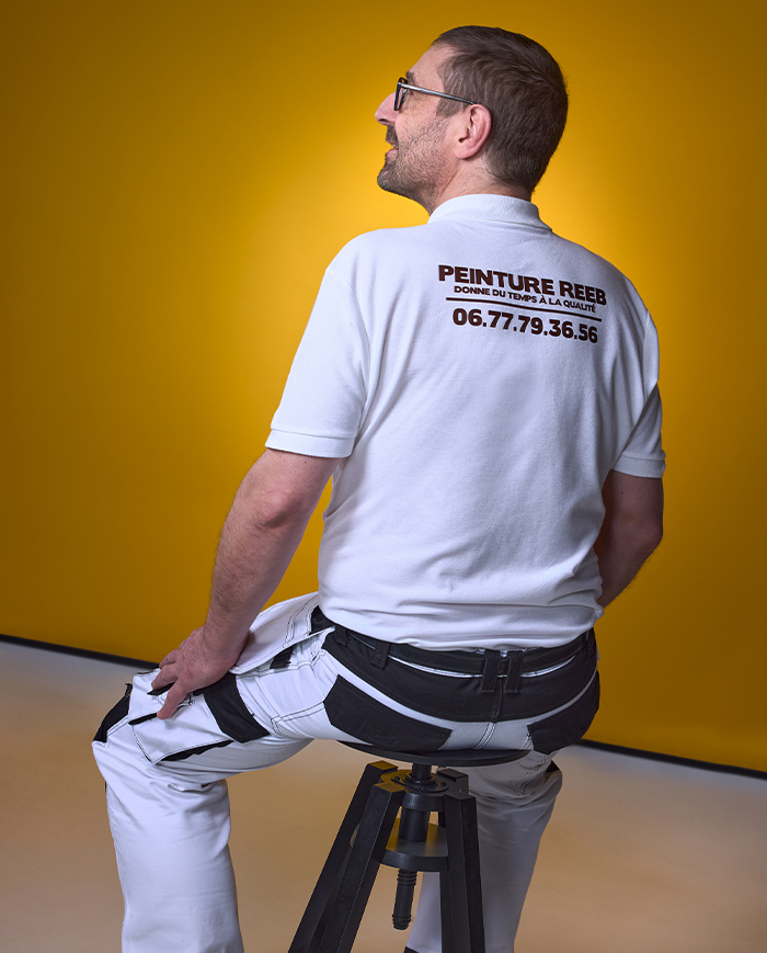 André Reeb – Artisan peintre à Mulhouse, Peinture Reeb Vue de dos d’André Reeb, artisan peintre à Mulhouse, portant un polo avec le logo et le numéro de Peinture Reeb