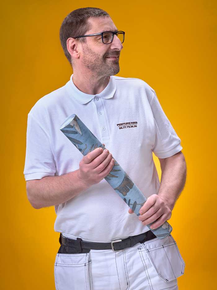 Portrait d’André Reeb, artisan peintre à Mulhouse, tenant un rouleau de papier peint décoratif